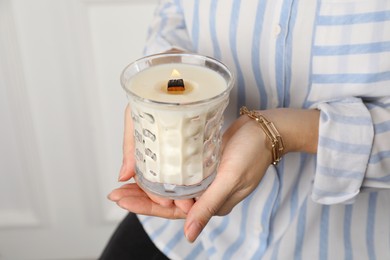 Woman with stylish jewelry holding burning soy candle on light background, closeup