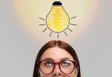 Image of Idea generation. Woman looking at illustration of glowing light bulb over her on light background