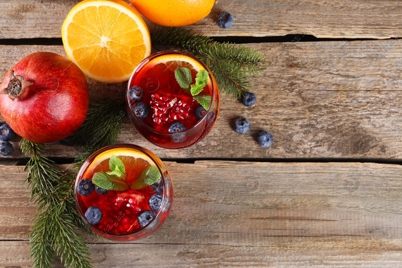 Photo of Aromatic Christmas Sangria drink in glasses, fir branches and ingredients on wooden table, flat lay. Space for text