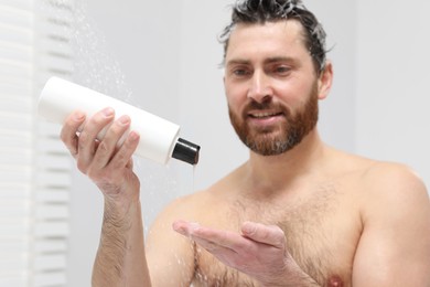Photo of Handsome man pouring shampoo onto his hand in shower