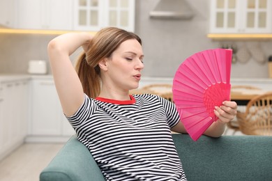 Photo of Woman waving pink hand fan to cool herself on sofa at home'