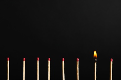 Row of matchsticks with burning one on black background. Be different