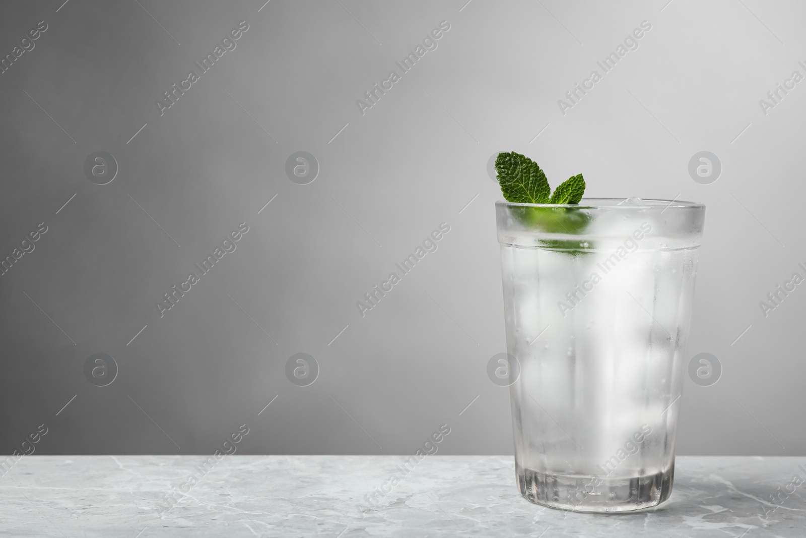 Photo of Glass of soda water with ice and mint on grey table. Space for text