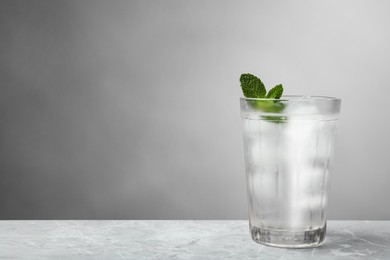 Glass of soda water with ice and mint on grey table. Space for text