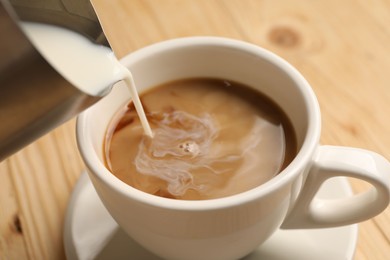 Photo of Pouring milk into cup with coffee at light wooden table, closeup