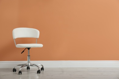 Photo of Modern office chair near orange coral wall indoors. Space for text