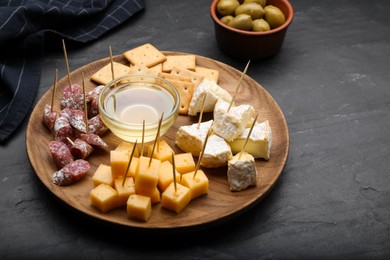 Photo of Toothpick appetizers. Pieces of cheese, sausage and honey on black table