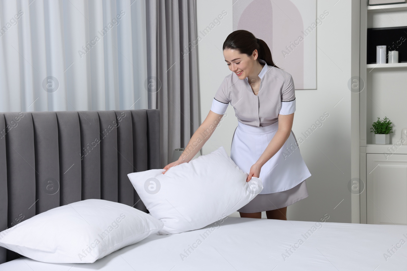 Photo of Young maid making bed in hotel room