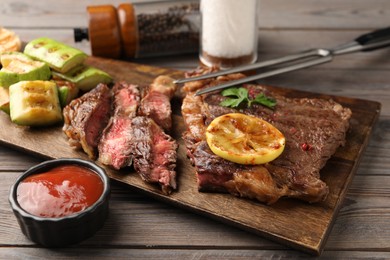 Photo of Delicious grilled beef steak and vegetables served on wooden table, closeup