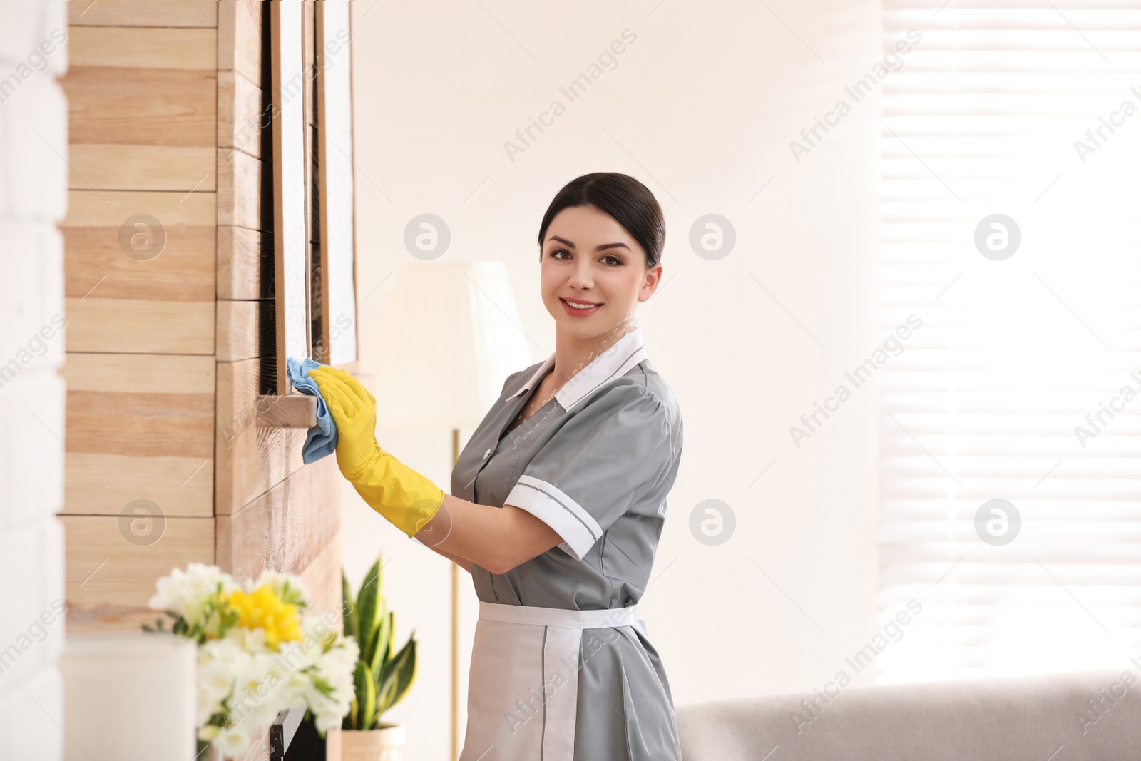 Photo of Young chambermaid wiping dust from furniture in hotel room