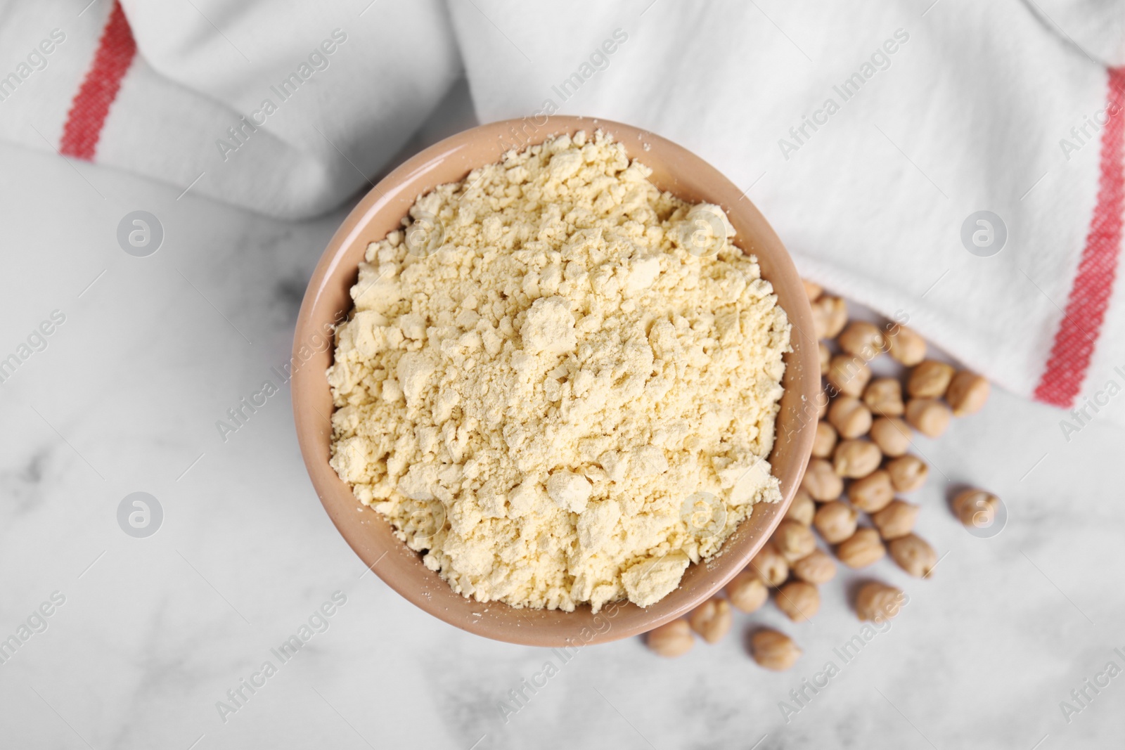 Photo of Chickpea flour in bowl and seeds on white marble table, top view