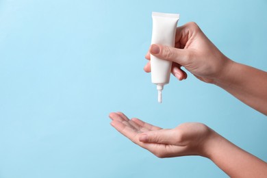 Photo of Woman applying cosmetic cream from tube onto her hand on light blue background, closeup. Space for text