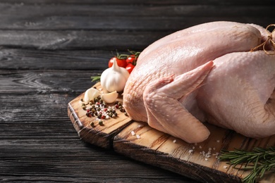 Photo of Board with raw turkey and ingredients on wooden background. Space for text