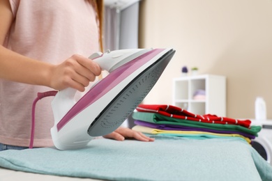 Young woman ironing clothes on board in bathroom, closeup. Space for text