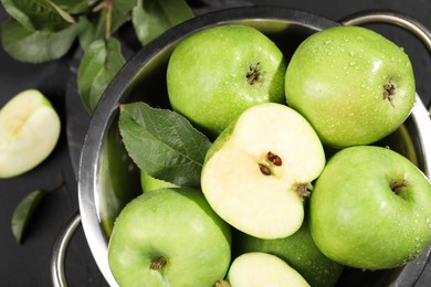 Photo of Ripe green apples with water drops and leaf in colander on table, top view