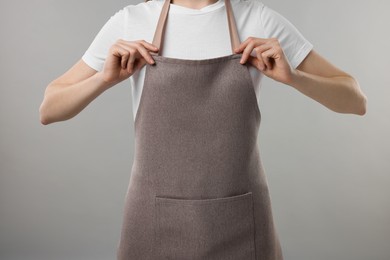 Photo of Woman wearing kitchen apron on grey background, closeup. Mockup for design