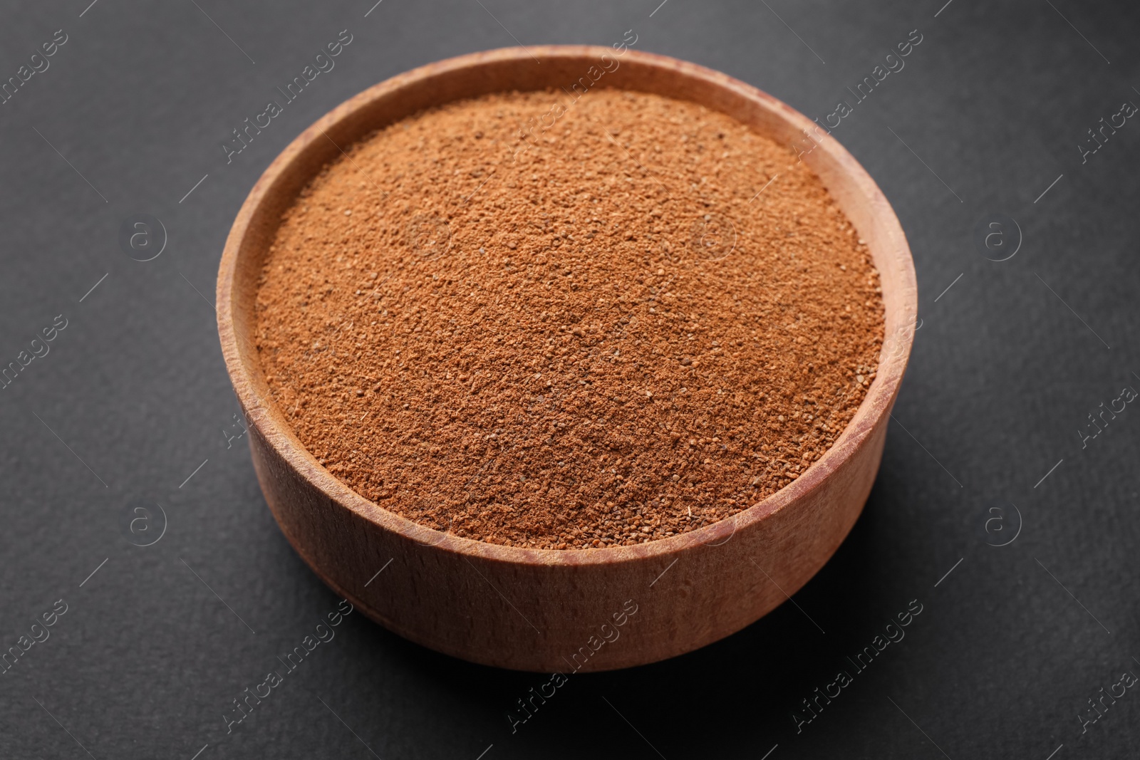 Photo of Aromatic cinnamon powder in wooden bowl on dark background