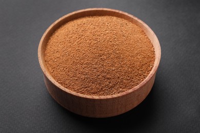 Aromatic cinnamon powder in wooden bowl on dark background