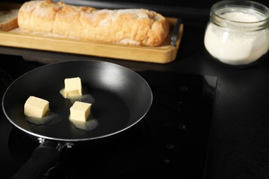 Photo of Melting butter in frying pan, bread and flour on black table