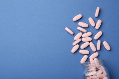 Bottle of pink vitamin capsules on blue background, top view. Space for text