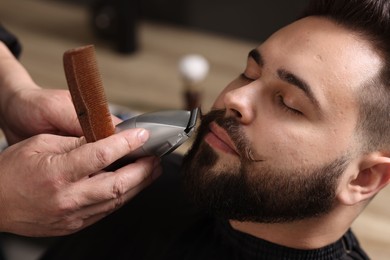 Professional barber trimming client's mustache in barbershop, closeup