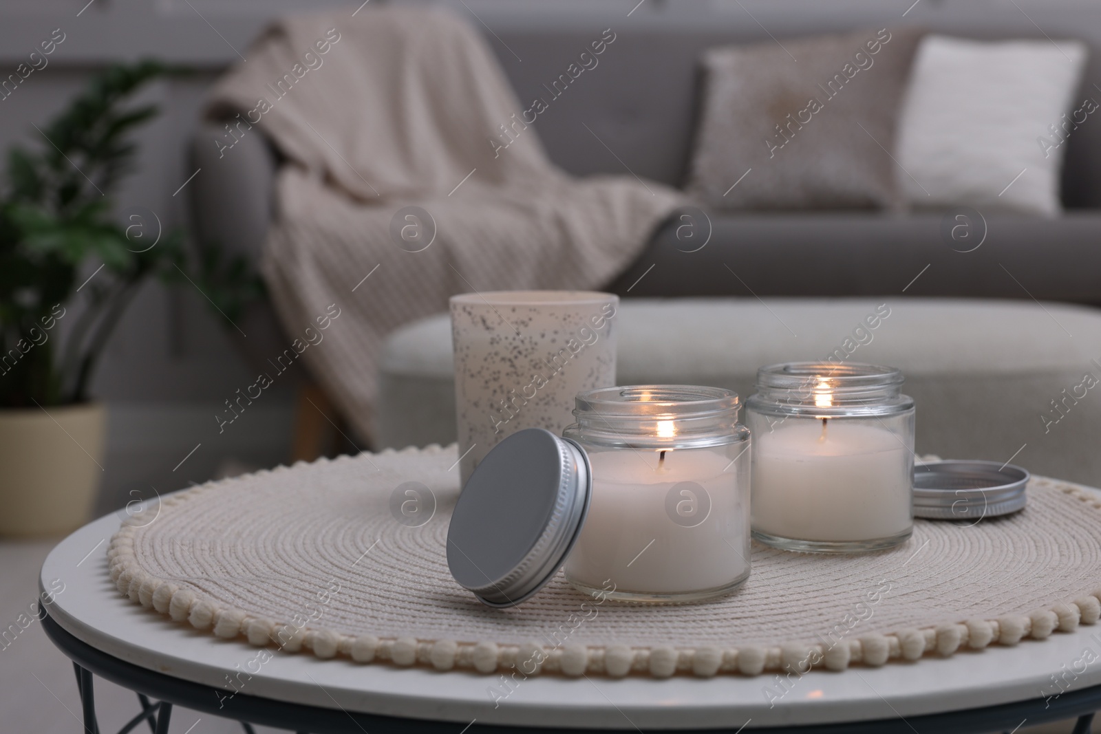 Photo of Burning candles in jars on white table indoors, space for text