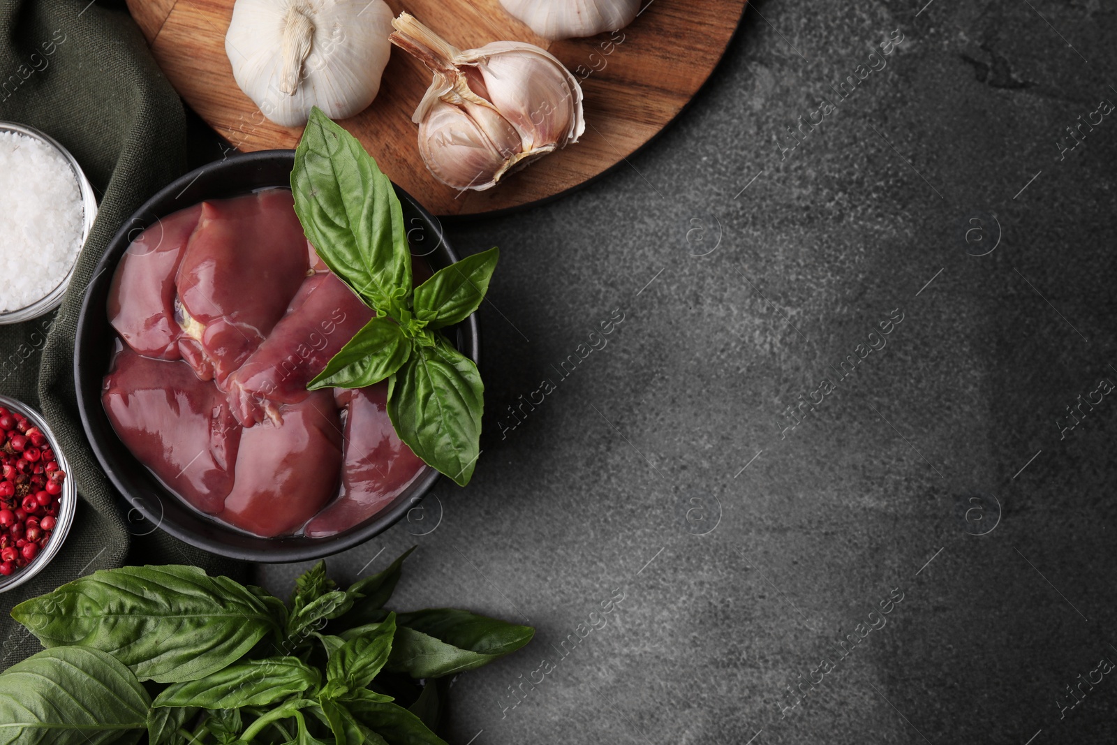 Photo of Bowl of raw chicken liver with basil and products on grey table, flat lay. Space for text
