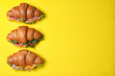 Photo of Tasty croissant sandwiches on yellow background, flat lay. Space for text