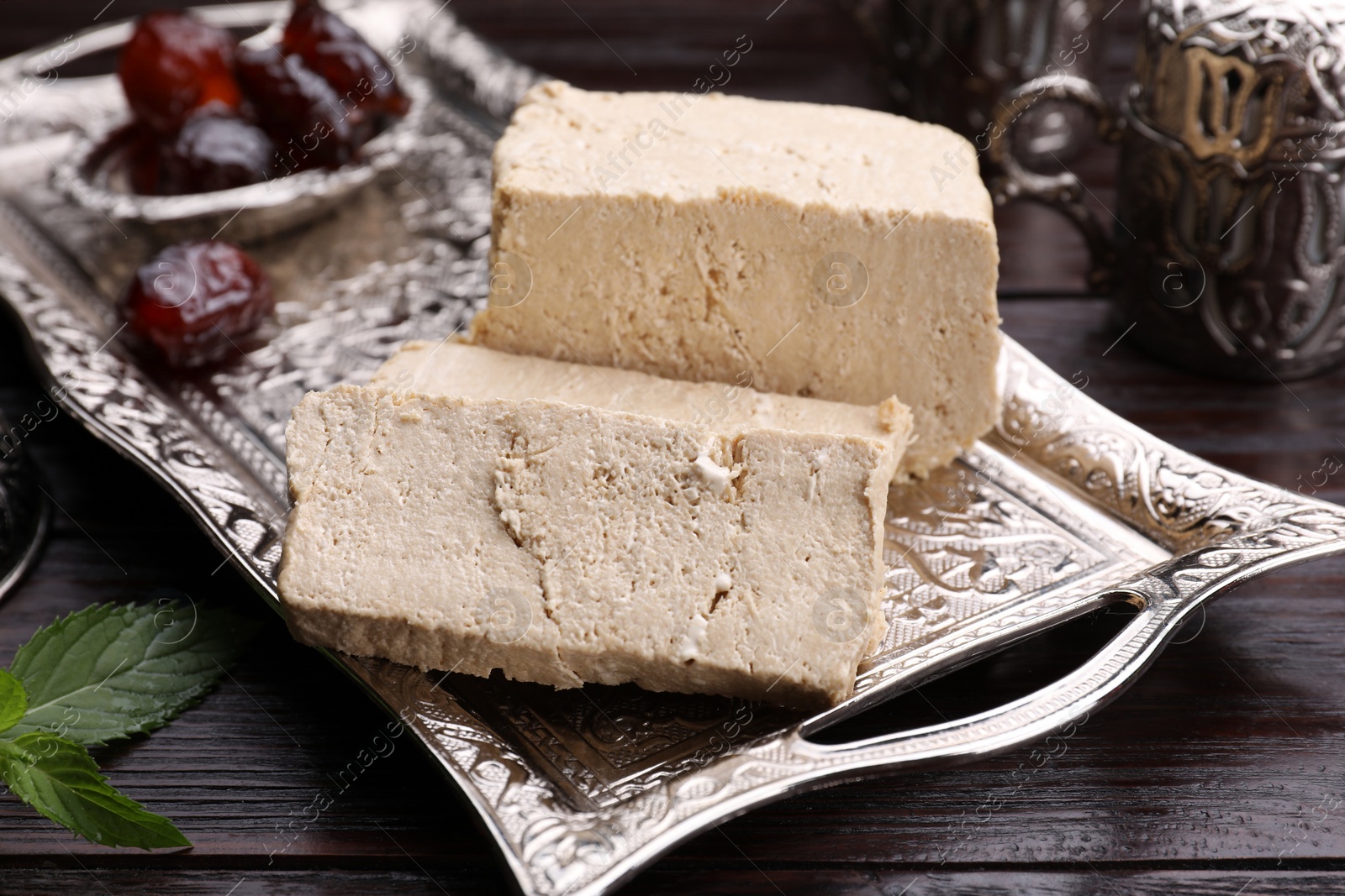 Photo of Pieces of tasty halva served on vintage tray on wooden table, closeup