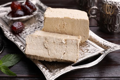 Photo of Pieces of tasty halva served on vintage tray on wooden table, closeup