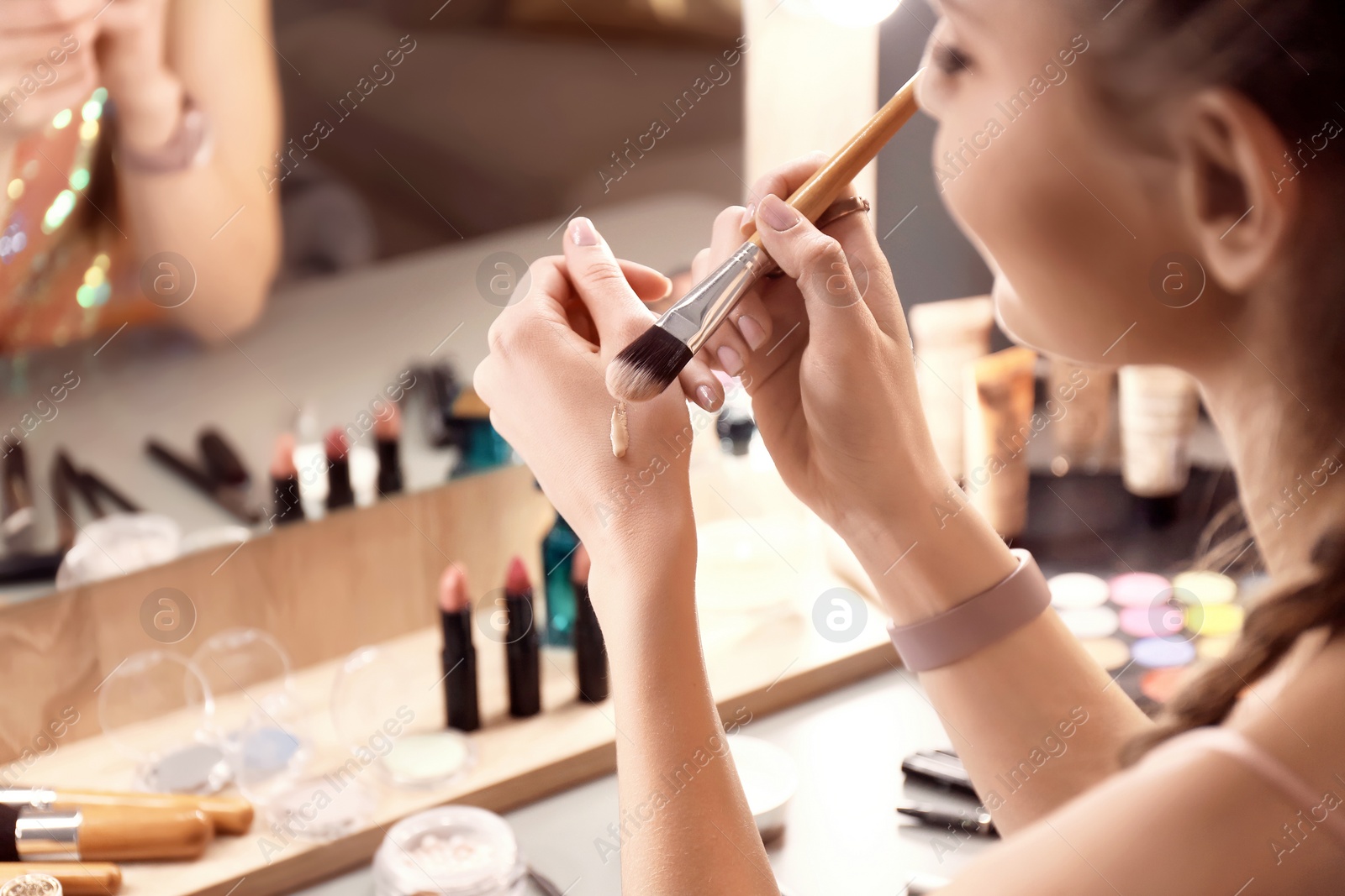 Photo of Young woman applying foundation on her hand in makeup room, closeup