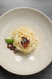 Tasty spaghetti with sun-dried tomatoes and parmesan cheese on grey table, top view. Exquisite presentation of pasta dish
