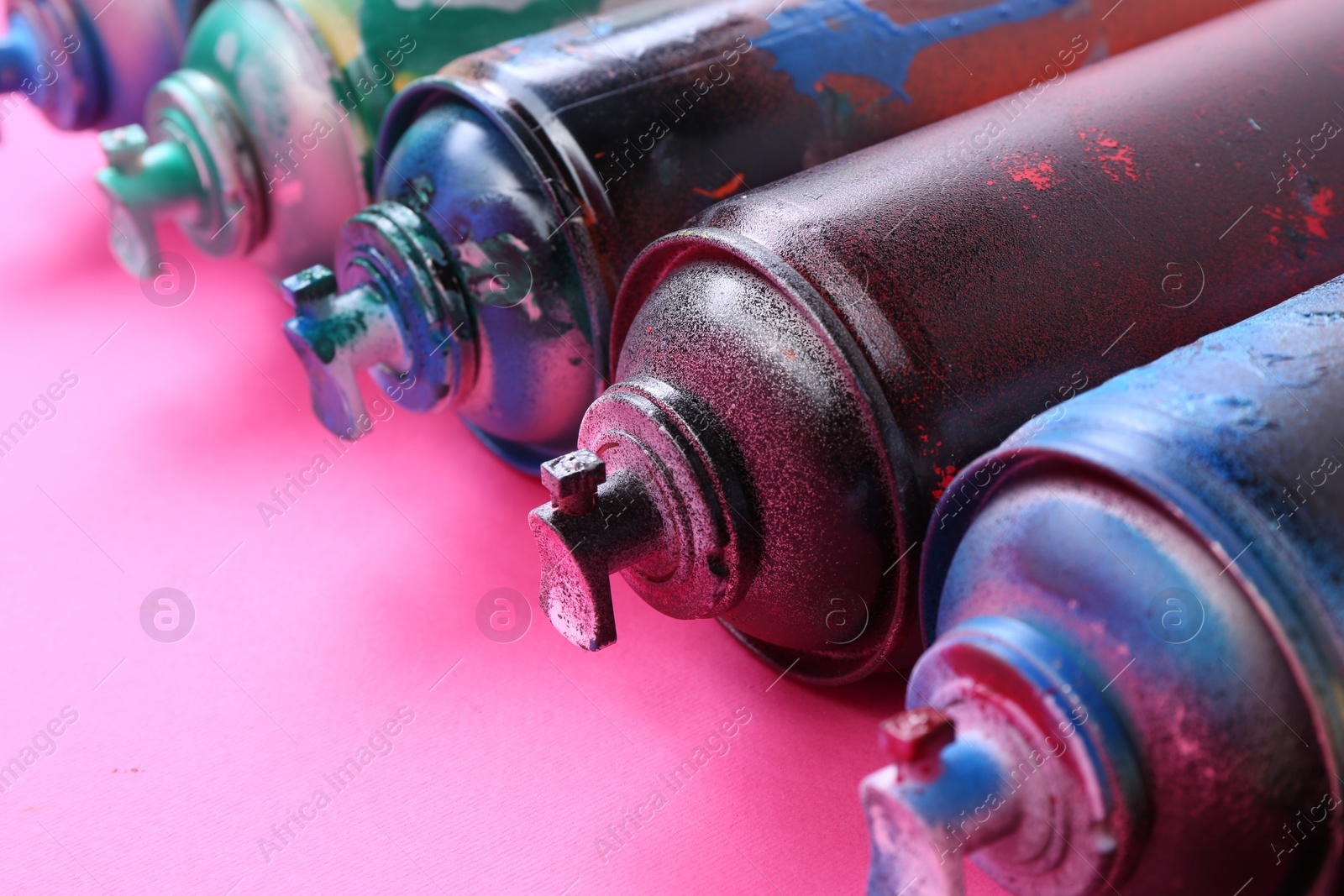 Photo of Many spray paint cans on pink background, closeup