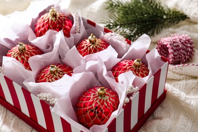 Photo of Beautiful red Christmas baubles in box on knitted plaid, closeup