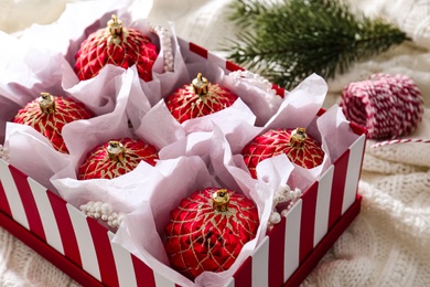 Beautiful red Christmas baubles in box on knitted plaid, closeup