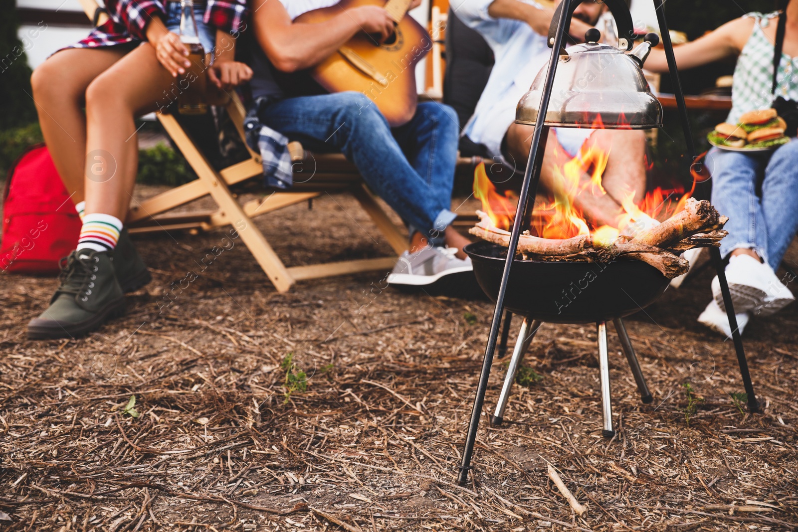 Image of Friends resting together near bonfire, closeup view. Camping season