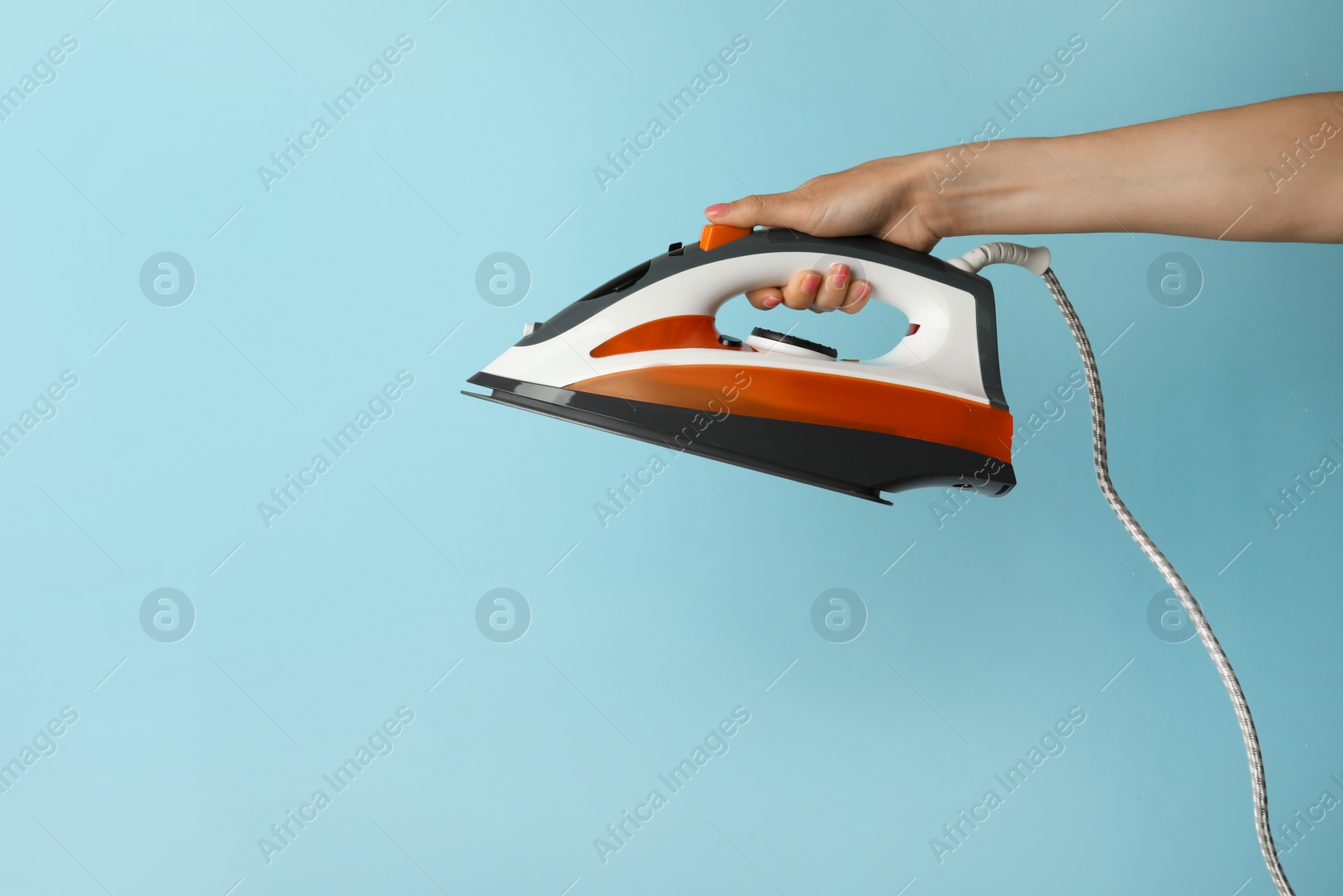 Photo of Woman holding modern iron on turquoise background, closeup. Space for text