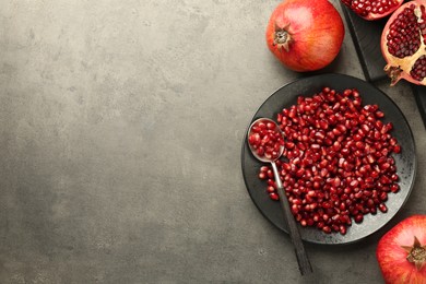 Photo of Ripe juicy pomegranates with grains on grey textured table, flat lay. Space for text