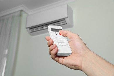 Photo of Man operating air conditioner with remote control indoors, closeup