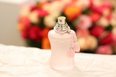 Bottle of perfume on crumpled paper against beautiful roses, closeup