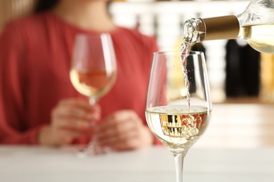 Photo of Woman at table in restaurant, focus on pouring wine into glass, closeup