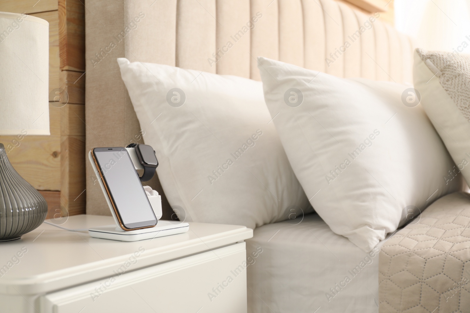 Photo of Different gadgets charging on wireless pad in bedroom