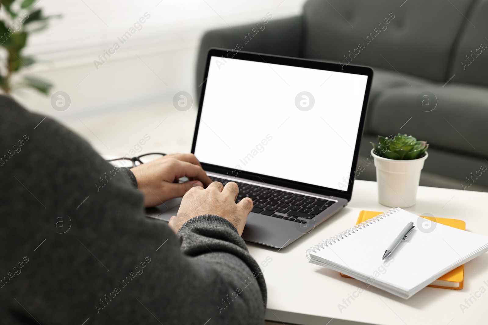 Photo of E-learning. Young man using laptop at white table indoors, closeup