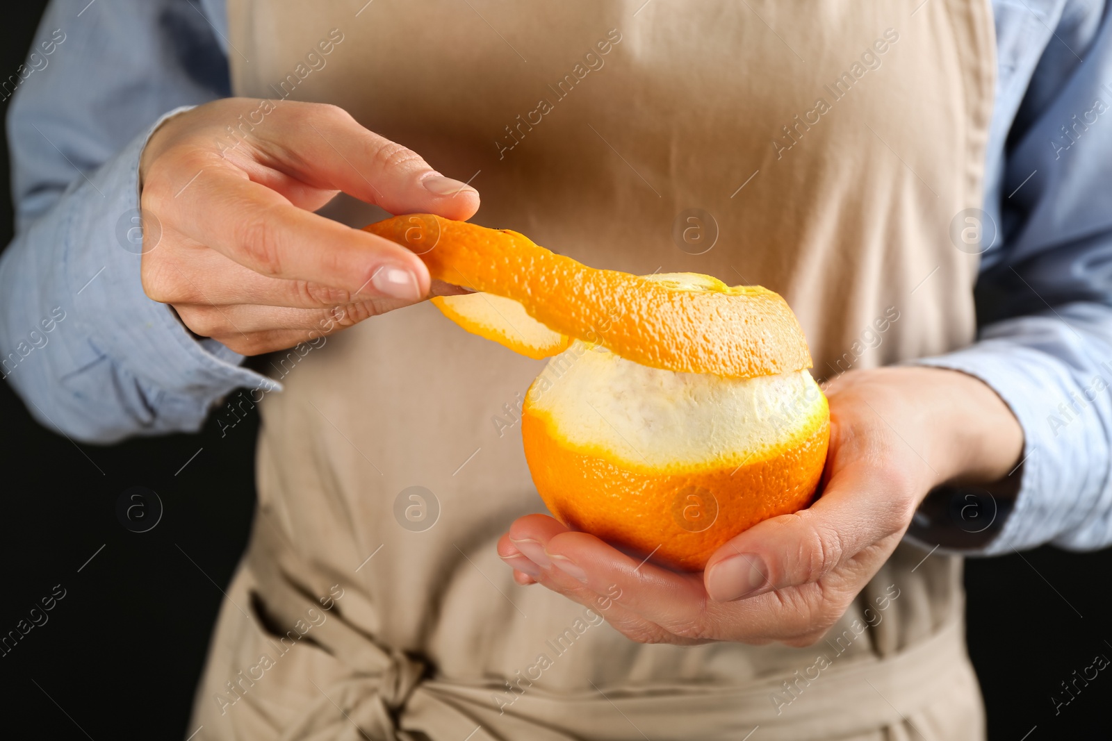 Photo of Woman peeling fresh orange on black background, closeup