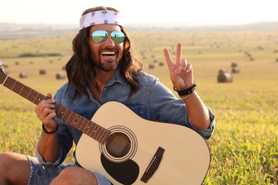 Photo of Happy hippie man with guitar showing peace sign in field