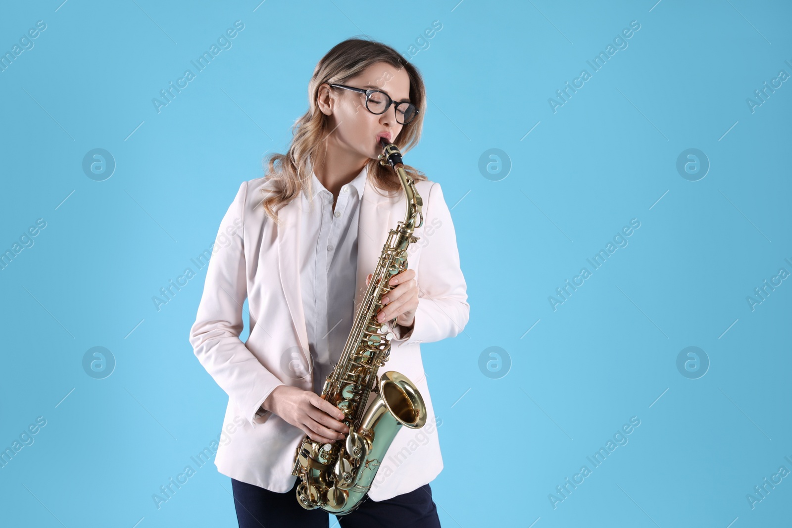 Photo of Beautiful young woman in elegant outfit playing saxophone on light blue background