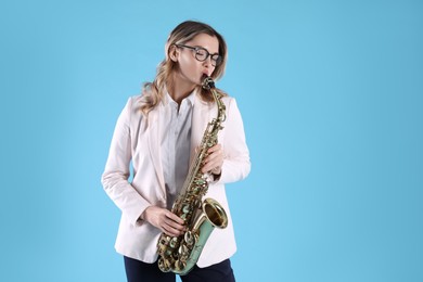 Beautiful young woman in elegant outfit playing saxophone on light blue background