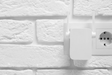 Photo of Wireless Wi-Fi repeater on white brick wall, space for text