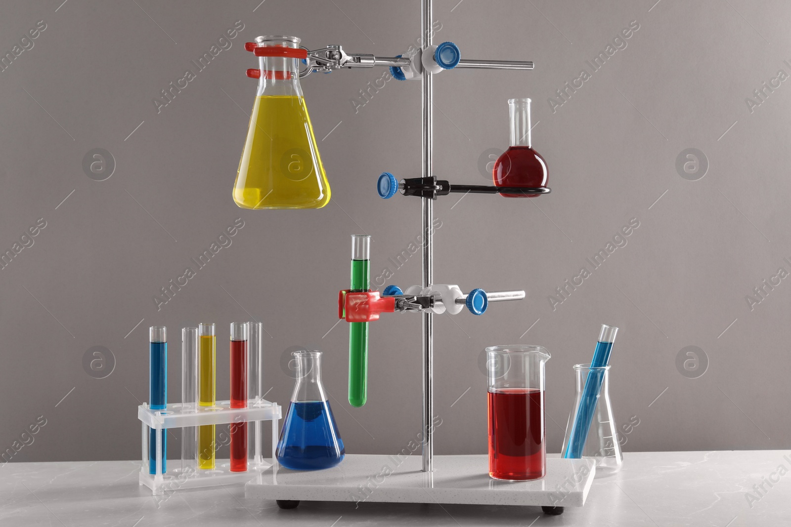 Photo of Retort stand and laboratory glassware with liquids on table against light grey background