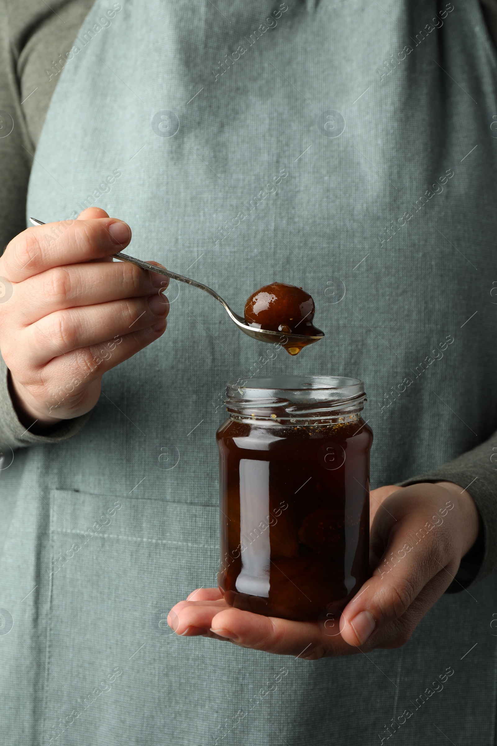 Photo of Woman holding jar of tasty sweet fig jam, closeup